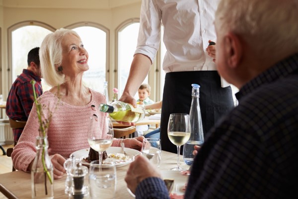 Waiter Serving Wine To Senior Couple In Restaurant